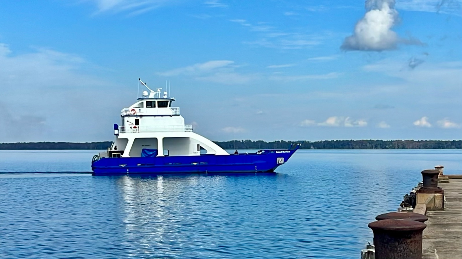 The Island Hot Shot crossing calm water with a low green shoreline behind